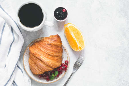 Continental breakfast with fresh croissant, berries, jam, black coffee and orange wedge on a table. Top view, copy space for your textの写真素材