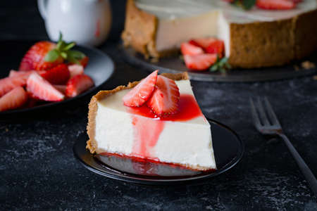 Cheesecake with fresh strawberries and strawberry syrup on black plate.の写真素材