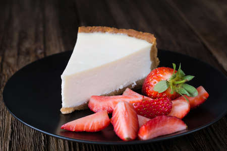 Cheesecake with fresh strawberries on black plate. Slice of plain cheesecake. Wooden table backgroundの写真素材
