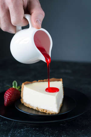 Cheesecake with sauce. Pouring strawberry sauce over plain cheesecake. Selective focus. Cheesecake with syrupの写真素材