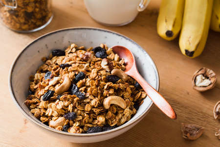 Granola with raisins and nuts in bowl. Breakfast with banana granola on wooden tableの写真素材