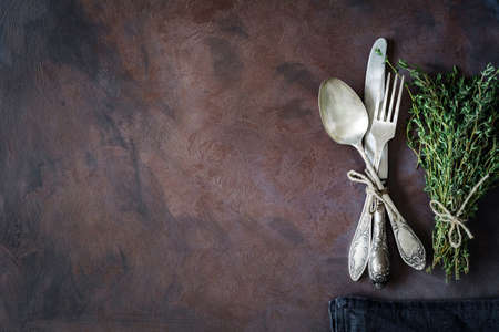 Vintage cutlery silverware on a dark textile and bunch of fresh thyme on a dark rusty background. Top view, copy space for text.の写真素材