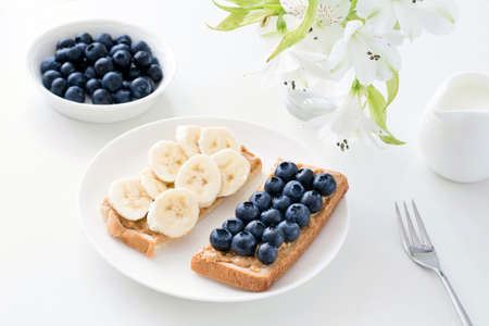 Healthy snack, healthy breakfast: two toasts with peanut butter spread, blueberries and bananas on white tableの写真素材