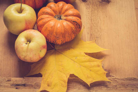 Pumpkin, apples and yellow fallen maple leaf on a wooden table with copy spaceの写真素材