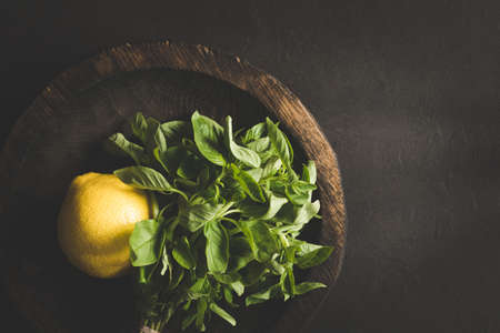 Fresh basil leaves and lemon on wooden plate over dark background. Top view with copy space, toned image. Concept of summer, freshness and fresh food ingredientsの写真素材