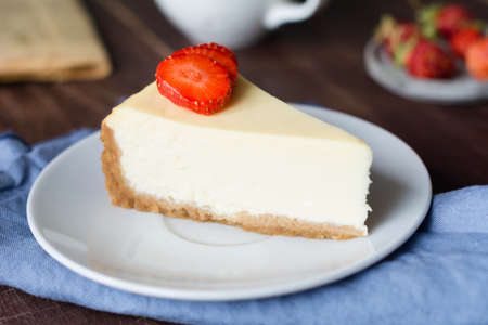 Slice of plain new york cheesecake with fresh strawberries, cup of coffee and newspaper on wooden table. Breakfast, lunch or snack at cafeの写真素材