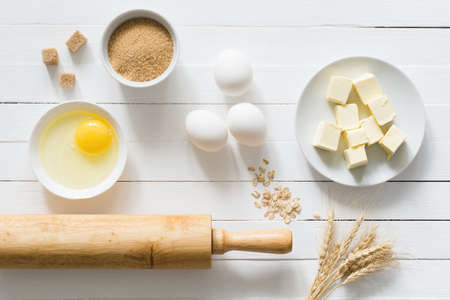 Baking ingredients: brown sugar, white eggs, rolling pin, wheat ears and butter on white wooden table. Top viewの写真素材