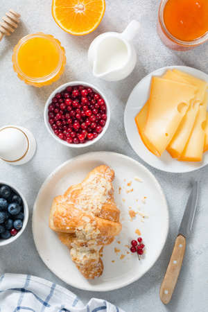 Continental breakfast table top view. Fresh croissants, boiled egg, cheese, orange, jam, honey, cream, blueberries and currants on bright blue table. Verticalの写真素材