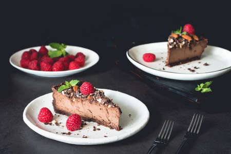 Two pieces of chocolate cheesecake decorated with raspberries and mint on dark background. Horizontal compositionの写真素材