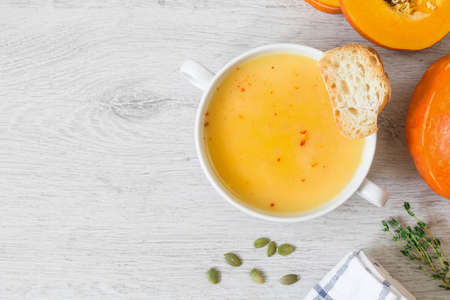 Pumpkin cream soup with red pepper flakes and toasted bread in bowl on grey background. Top view copy space for textの写真素材