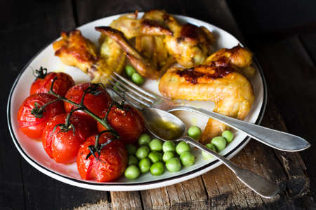 Spicy chicken wings, roasted cherry tomatoes and sauteed green peas on white plate. Baslanced meal. Closeup view, selective focusの写真素材