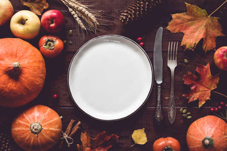 Autumn Halloween or thanksgiving day table setting. Fallen leaves, pumpkins, spices, empty plate and vintage cutlery on wooden table. Top view, toned imageの写真素材
