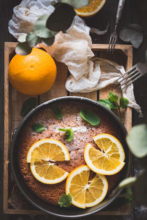 Orange cake decorated with orange slices and mint leaf on wooden tray. Top view. Food still lifeの写真素材