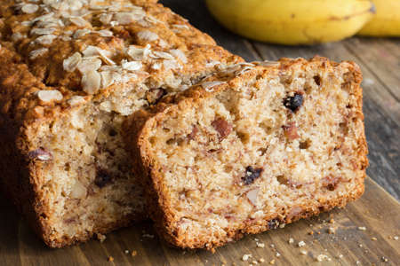 Homemade banana bread loaf with walnuts sliced on wooden cutting board. Closeup view, horizontalの写真素材
