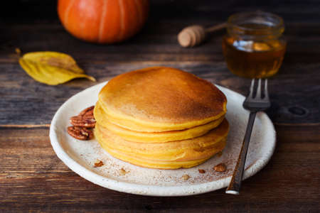 Pumpkin pancakes stack on white plate on wooden table. Closeup view. Morning sunlightの写真素材