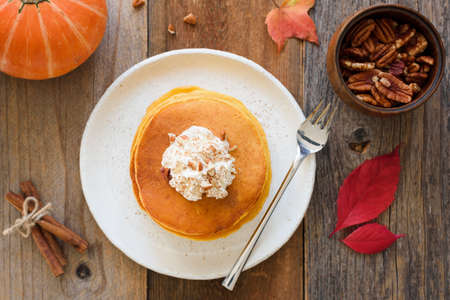 Pumpkin pancakes with whipped cream and cinnamon on wooden table. Top view, horizontalの写真素材