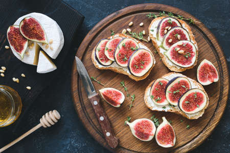 Bruschetta with fresh purple figs, ricotta cheese and honey on wooden cutting board served with brie camambert cheese and decorated with thyme. Healthy gourmet snackの写真素材