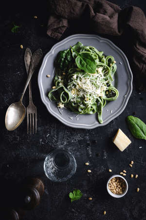 Green spinach pasta with cheese and pine nuts. Top view, dark food photo. Vertical. Homemade healthy green pastaの写真素材