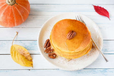 Homemade pumpkin pancakes with honey and pecan nuts on white plate over bright background. Horizontal view. Seasonal autumn foodの写真素材