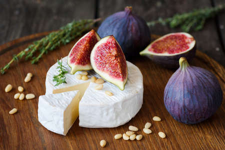 Camembert cheese with fresh purple figs, thyme and pine nuts on cutting boardの写真素材