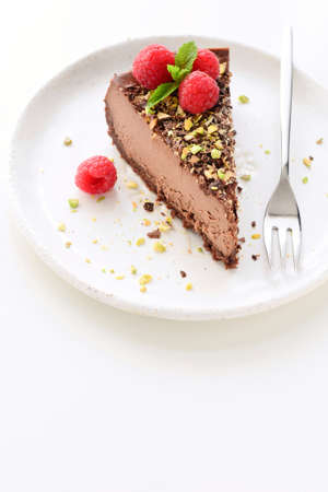 Chocolate cheesecake or slice of chocolate cream pie decorated with raspberries and crushed nuts on...