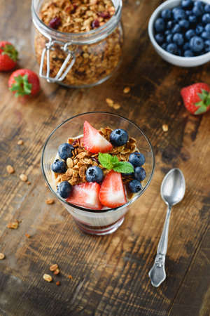 Granola with strawberries, blueberries and yogurt in a glass. Healthy breakfast food. Wooden table backgroundの写真素材