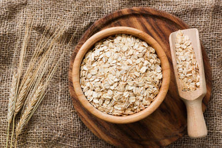 Rolled oats, organic oat flakes in wooden bowl and golden wheat ears on wooden background. Healthy lifestyle, healthy eating, vegan food conceptの写真素材