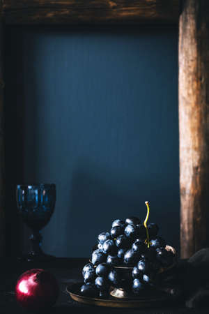 Still life of black grapes on vintage tray over blue background. Vertical, retro style, copy space for textの写真素材