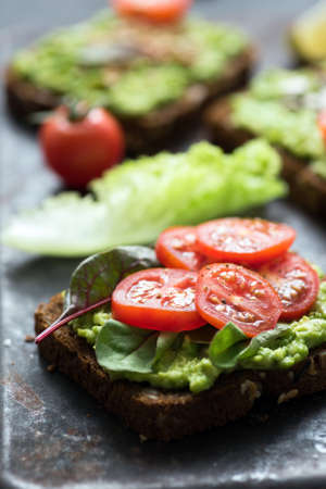 Toast with avocado, spinach and cherry tomato on whole grain rye bread. Closeup view, selective focusの写真素材