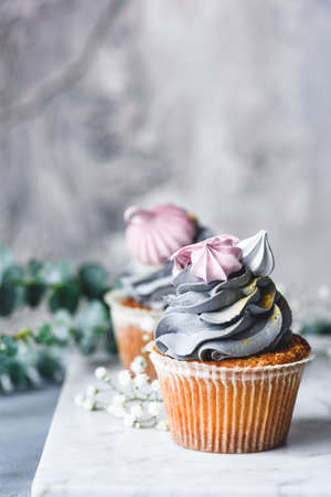 Cakes with gray pastel cream and mini pink meringues on marble surface over concrete background. Pastel colors. Closeup view, selective focusの写真素材