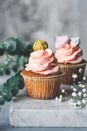 Cupcakes with coral cream and golden decorations on a marble board table. Wedding cupcakes. Toned image, selective focusの写真素材