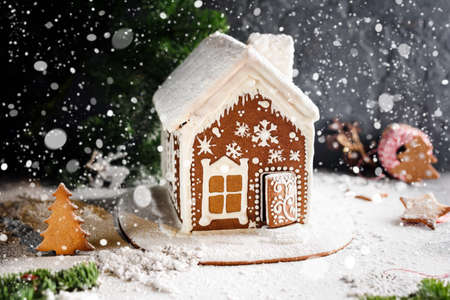 Homemade gingerbread house, falling snow and festive Christmas decorations. Christmas card, winter still life. Copy space for textの写真素材