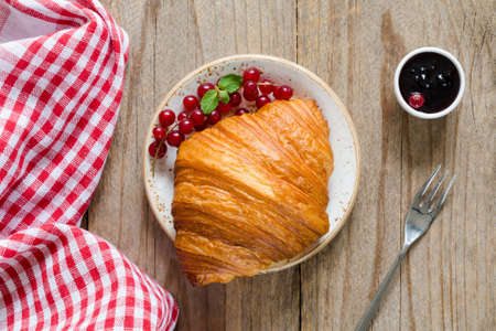 Croissant with fresh berries and jam on old wooden table. Top view, horizontal