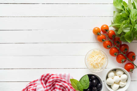 Italian food ingredients for cooking on white table. Parmesan cheese, cherry tomatoes, olives, mozzarella cheese and basil. Pizza ingredientsの写真素材