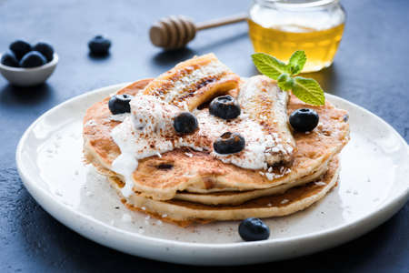 Oat pancakes with greek yogurt, roasted banana, blueberries and cinnamon on white plateの写真素材