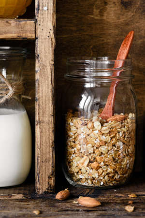 Homemade granola in jar and bottle of milk. Rustic kitchen pantry. Vertical, toned image