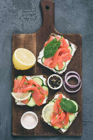 Toast sandwiches with salmon, cucumber and cream cheese on old cutting board. Table top view, toned imageの写真素材