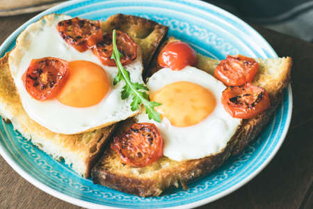 Breakfast toast with egg, roasted tomatoes and arugula salad on blue plate. Closeup viewの写真素材