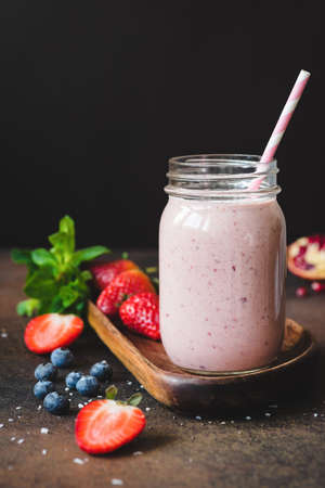 Strawberry smoothie in a jar with drinking straw on dark background. Copy space for text, vertical...