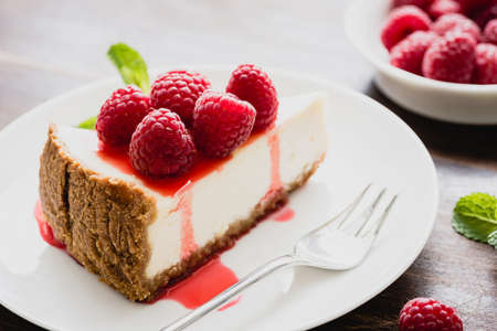 Cheesecake with raspberries and berry sauce on white plate, closeup view, selective focus. Slice of cheesecakeの写真素材