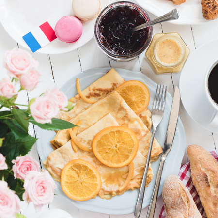 French breakfast Crepes Suzette, baguette, coffee and jam on white wooden table. French flag, macarons, jam, honey and roses asideの写真素材