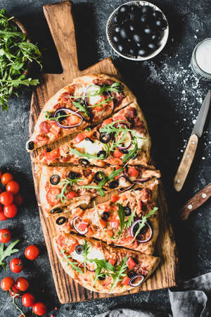 Flatbread pizza garnished with fresh arugula on wooden pizza board, top view, vertical compositionの写真素材