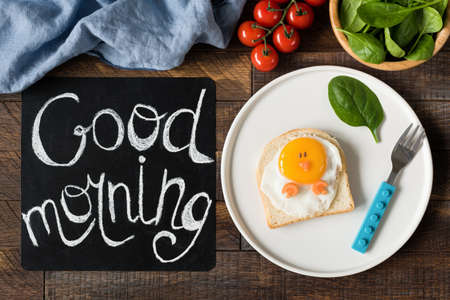 Funny sandwich chicken for kids on a plate. Black chalkboard with Good morning greeting, Healthy breakfast and healthy eating concept. Wooden table backgroundの写真素材