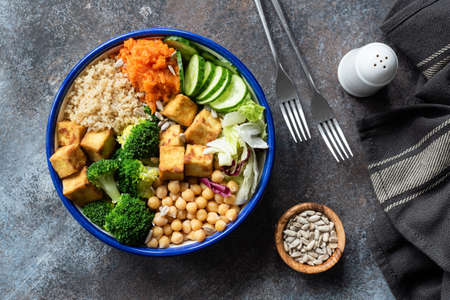 Colorful Buddha bowl on dark background, top view. Buddha bowl with quinoa, tofu, broccoli, sweet potato, chickpea and cucumber. Healthy vegetarian salad bowlの写真素材