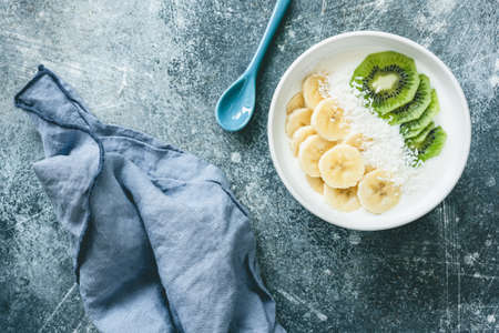 Yogurt with banana, kiwi and coconut bowl. Vegan yogurt with fruits. Healthy eating, dieting, fitness, healthy lifestyle concept. Table top viewの写真素材