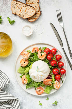 Healthy salad with burrata, shrimps, tomato and lettuce on white plate. Top view of tasty italian salad with olive oil dressing. Healthy eating conceptの写真素材