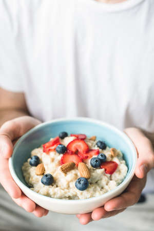 Bowl of oatmeal porridge with berries in hands. Vegetarian, healthy lifestyle, healthy eating concept. Selective focus and copy space for textの写真素材