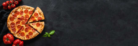 Tasty pepperoni pizza and cooking ingredients tomatoes basil on black concrete background. Top view...