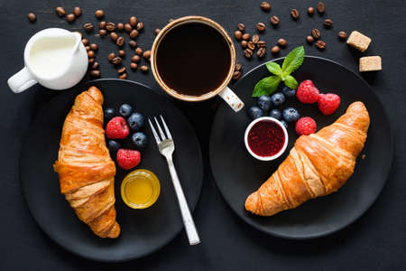 Breakfast with croissants, honey, jam, black coffee, cream and fresh berries on black background. Top view, flat lay compositionの写真素材