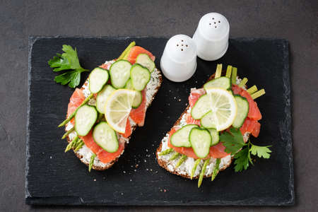 Asparagus and salmon sandwiches on a slate background. Tasty sandwich with smoked salmon, cream cheese, asparagus and cucumber